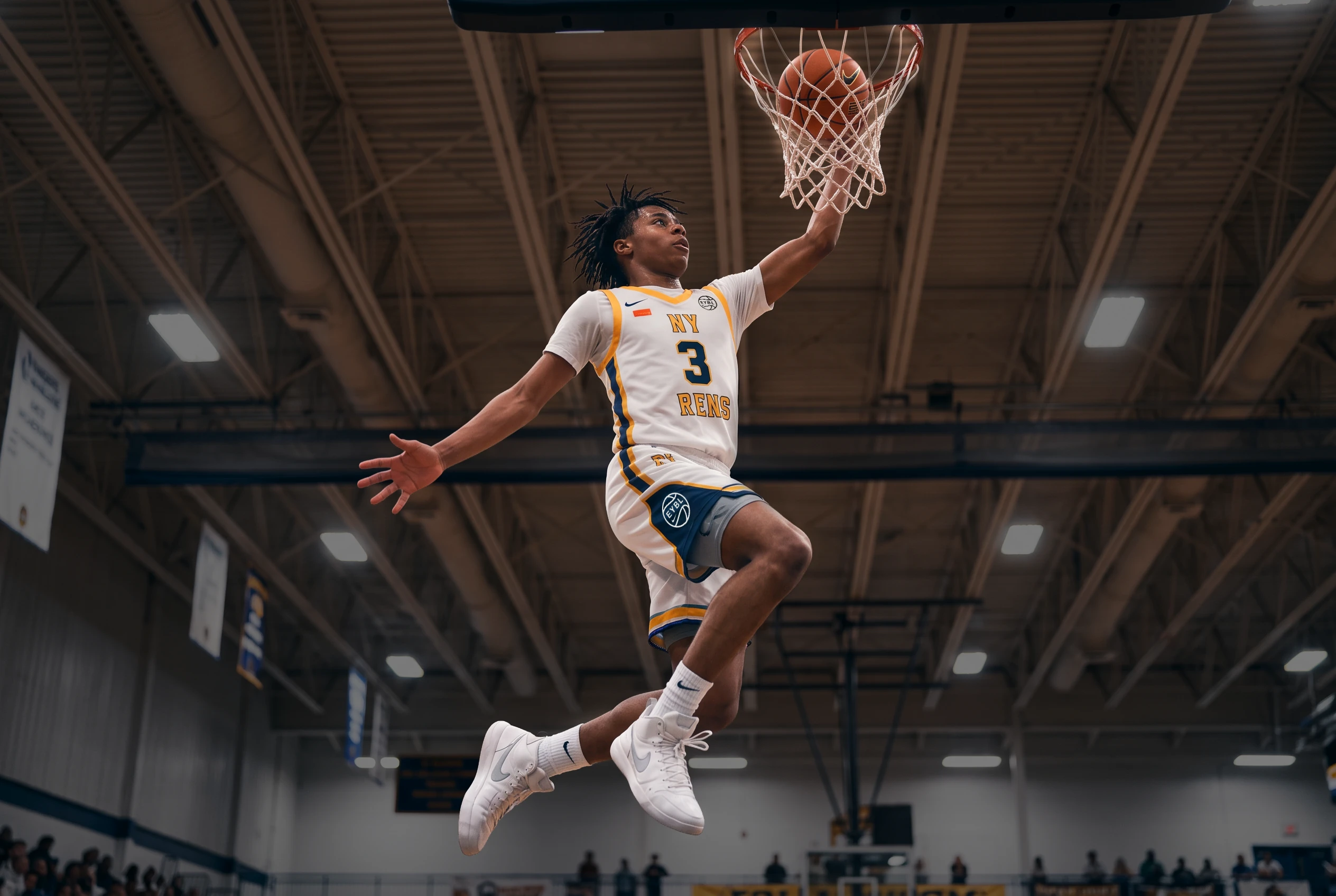 A teenage NY Rens player in a white and gold number 3 jersey leaping toward the basket